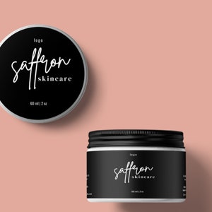 May include: Two black and white skincare jars with lids. The jars have the words "saffron skincare" in a cursive font. The top jar is round, and the bottom jar is cylindrical. The jars are labeled "60 ml | 2 oz".
