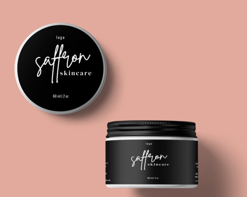 May include: Two black and white skincare jars with lids. The jars have the words "saffron skincare" in a cursive font. The top jar is round, and the bottom jar is cylindrical. The jars are labeled "60 ml | 2 oz".