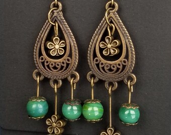 May include: A pair of dangle earrings with a bronze filigree design and green glass beads. The earrings have a floral motif and are suspended from a hook.