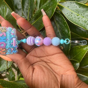 May include: A blue and pink beaded key chain with a charm that says "Nurse" in glitter. The charm is decorated with a heart, a syringe, and a leopard print.