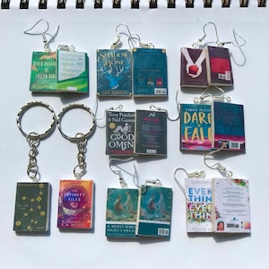 May include: A selection of miniature book earrings and keyrings. The earrings and keyrings feature book covers with titles such as "The Seven Husbands of Evelyn Hugo" and "Shadow and Bone." The earrings have silver hooks, and the keyrings have silver rings.