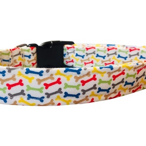 May include: A white dog collar with a colorful bone pattern. The collar has a black plastic buckle.