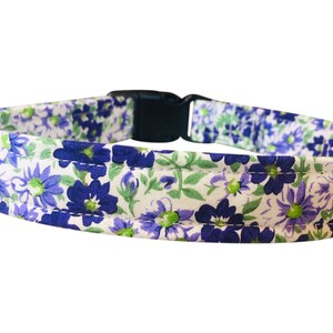May include: A white dog collar with a purple and green floral pattern. The collar has a black plastic buckle.