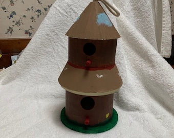 May include: A three-tiered birdhouse with a brown base and a green base. The birdhouse has two openings for birds to enter. The birdhouse is painted with white and blue accents.