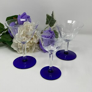 May include: Three clear glass cocktail glasses with etched designs on the bowl. The glasses have blue bases.