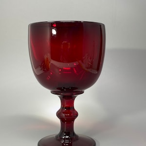 Könnte beinhalten: Ein tiefroter Glaskelch mit einem dicken Stiel und einer breiten Basis.