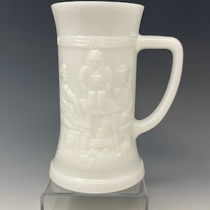 Puede incluir: Jarra de cerveza de cerámica blanca con un diseño en relieve de tres personas bebiendo en una mesa. La jarra tiene un asa y una base ancha.