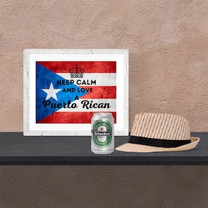 May include: A framed print of the Puerto Rican flag with the text "KEEP CALM AND LOVE A Puerto Rican." Next to it is a Heineken beer can and a straw fedora hat with a black band.
