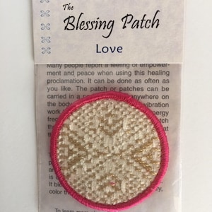 May include: A round, white fabric patch with gold embroidery and a pink border. The patch is labeled "The Blessing Patch Love".