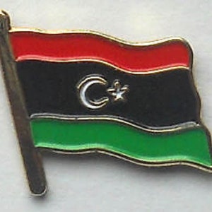 May include: A gold-coloured pin featuring a red, black and green Libyan flag. The flag has a crescent moon and star in the centre.