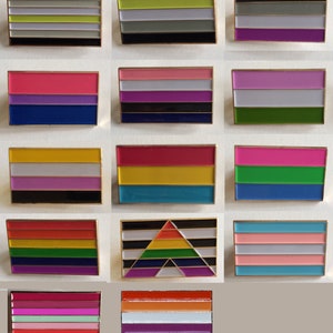 May include: A set of 12 enamel pins featuring different pride flags. The flags include the genderqueer, transgender, lesbian, bisexual, pansexual, non-binary, asexual, intersex, polyamorous, and genderfluid flags.