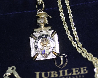 May include: A gold chain necklace with a pendant featuring a knight's helmet, crossed swords, and a skull and crossbones. The pendant is inscribed with "Knight of Pythias". The necklace is displayed on a blue velvet pouch with the text "Jubilee Fine Jewellers Since 1952".