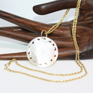 May include: A gold chain necklace with a large, round, white, mother-of-pearl pendant. The pendant has a delicate, intricate design with cutouts.