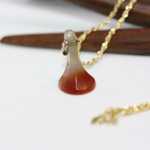 Puede incluir: Un collar de cadena dorada con un colgante de ágata roja y blanca. El colgante tiene forma de lágrima y un acabado liso y pulido.