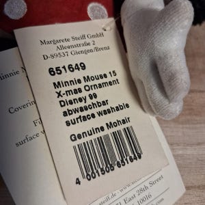 Pu&ograve; includere: Un ornamento natalizio di Minnie Mouse con un fiocco rosso a pois e un guanto bianco. L'etichetta recita "Minnie Mouse 15 X-mas Ornament Disney 99". L'ornamento &egrave; realizzato in mohair genuino.