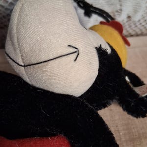 Pu&ograve; includere: Un peluche con un viso bianco, un dettaglio a freccia nera, pelliccia nera e un design a pois rossi e bianchi. Il giocattolo ha un cappello giallo e rosso. Il giocattolo &egrave; un personaggio dei cartoni animati classico.