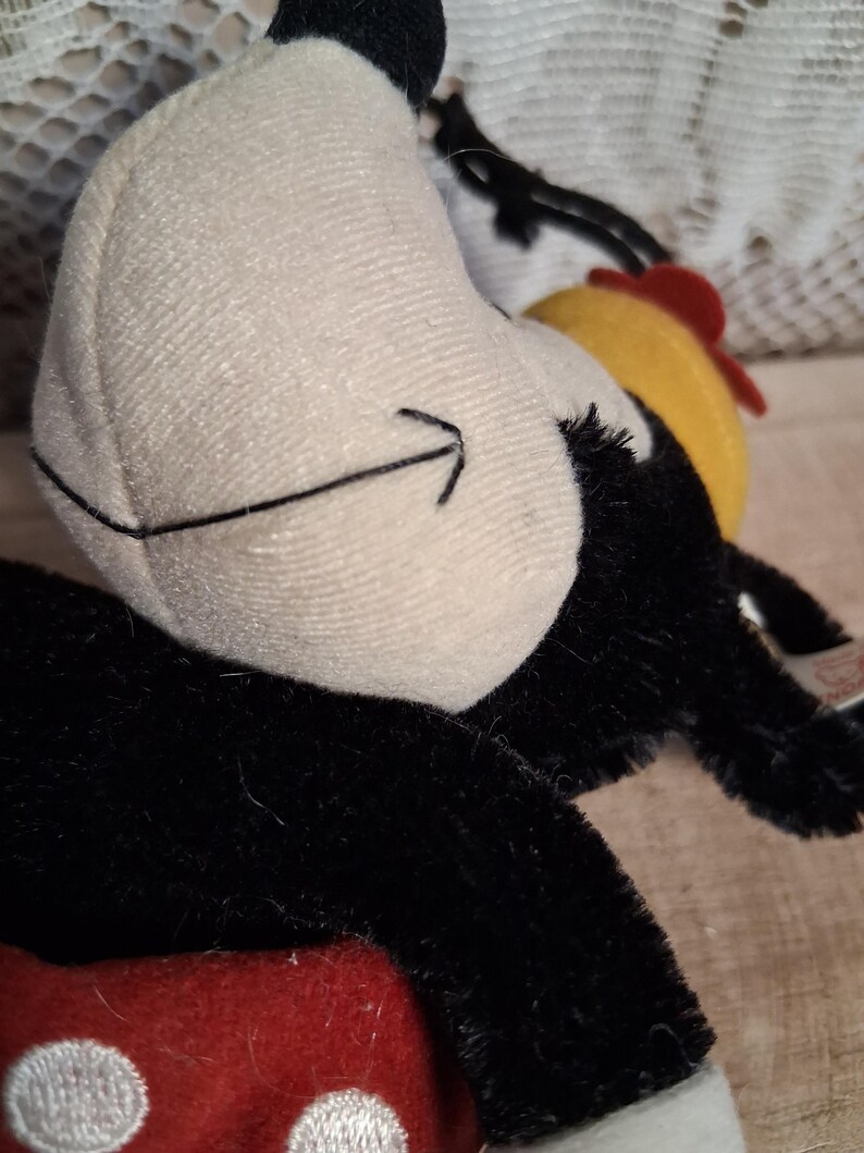 Pu&ograve; includere: Un peluche con un viso bianco, un dettaglio a freccia nera, pelliccia nera e un design a pois rossi e bianchi. Il giocattolo ha un cappello giallo e rosso. Il giocattolo &egrave; un personaggio dei cartoni animati classico.