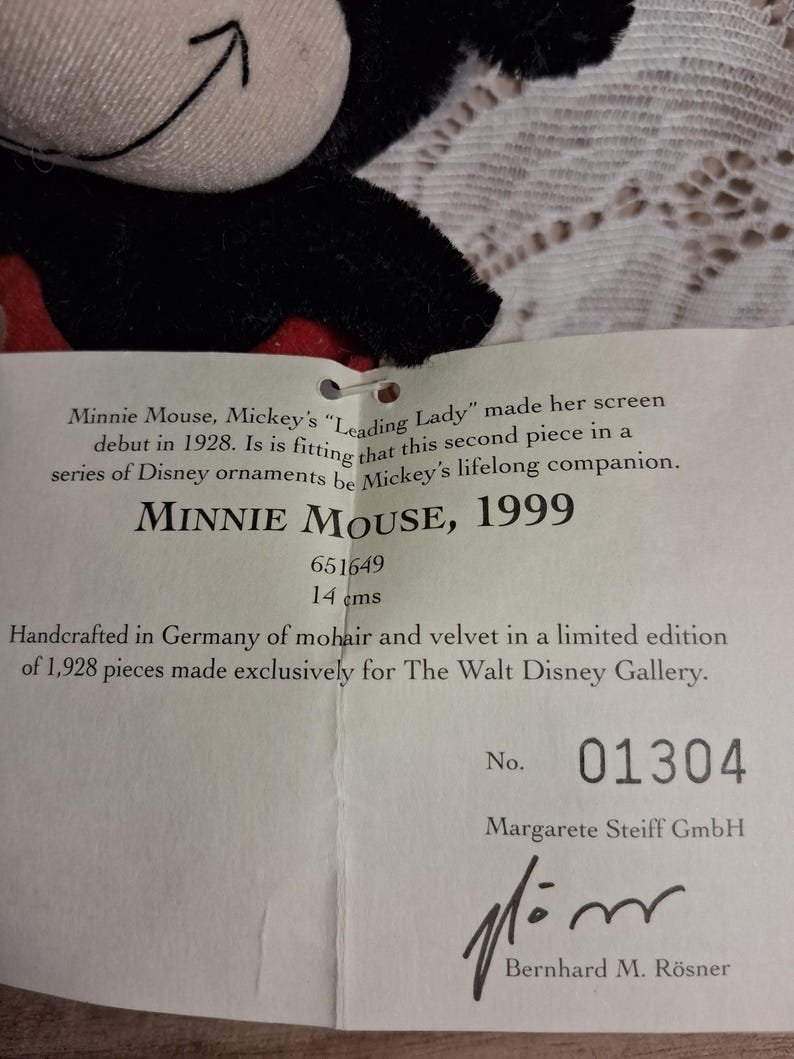 Pu&ograve; includere: Un peluche di Minnie Mouse con un abito nero e rosso. L'etichetta recita "MINNIE MOUSE, 1999" e "14 cm". L'etichetta indica anche che &egrave; stato realizzato a mano in Germania in mohair e velluto in edizione limitata.