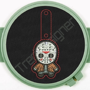 Puede incluir: Parche bordado con un personaje de dibujos animados con máscara de hockey. El diseño, en marrón, rojo y blanco, está sobre un fondo negro, dentro de un bastidor de bordado verde. El texto "TredDesigner" es visible. Ideal para ropa.