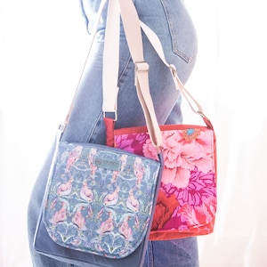 May include: Two canvas crossbody bags with adjustable straps. One bag has a floral print in shades of pink and red. The other bag has a blue background with a floral pattern in shades of pink and white. The text "The Pretty" is visible on the blue bag.