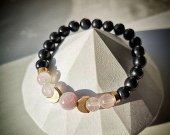 May include: A black beaded bracelet with gold crescent moon charms and pink rose quartz beads.