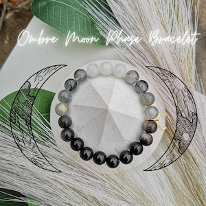 Peut inclure: Bracelet en phase de lune ombrée avec des perles noires, blanches et grises. Le bracelet est orné d'un charme en forme de croissant de lune doré.