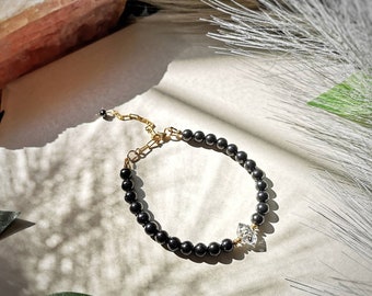 May include: A black beaded bracelet with a gold clasp and a clear crystal charm.