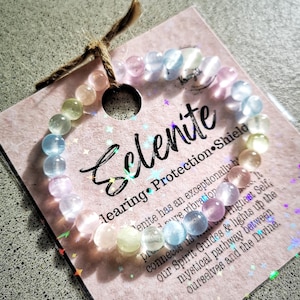 May include: A rainbow-coloured selenite crystal bracelet with a pink card that reads "Selenite Healing Protection Shield" and includes a description of the crystal's properties.