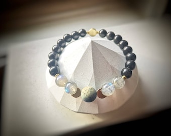 May include: A black beaded bracelet with gold accents and three larger beads, one green and two iridescent.