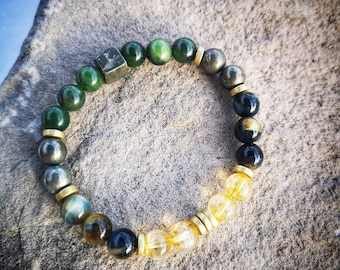 May include: A green, black, and gold beaded bracelet with a square pyrite charm. The bracelet is made with natural stones and is designed to be worn on the wrist.