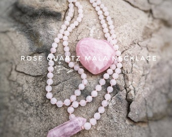 May include: A pink rose quartz mala necklace with a heart-shaped pendant and a pointed crystal pendant. The necklace is laid out on a textured gray surface. "ROSE QUARTZ MALA NECKLACE" is written in white text on the surface.