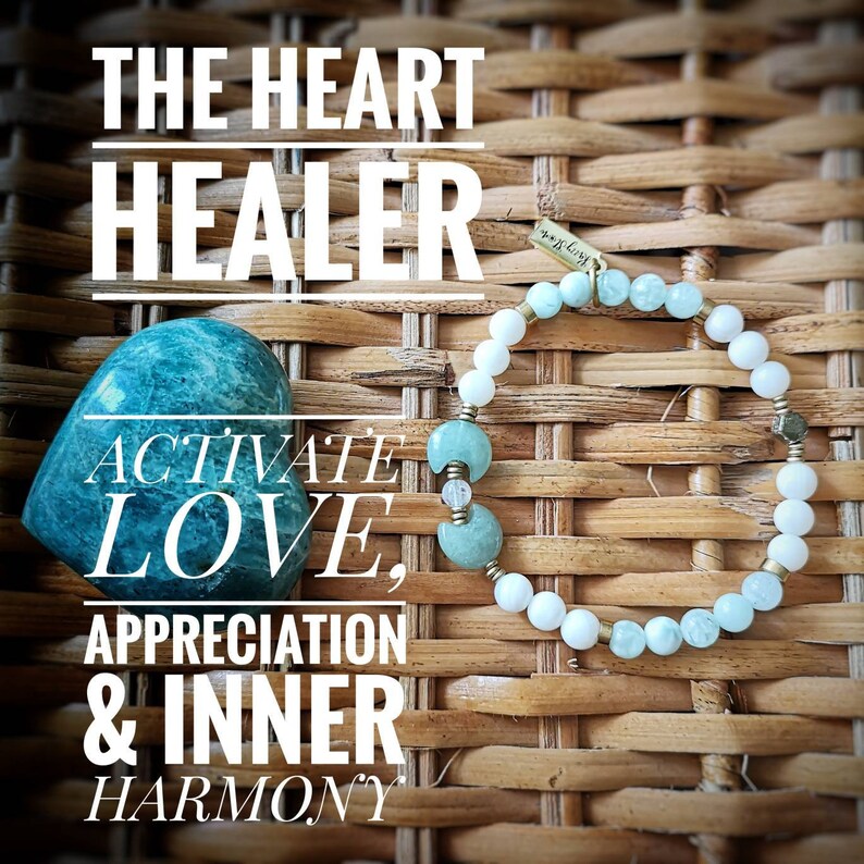 May include: A teal heart-shaped crystal with the text "Activate Love, Appreciation & Inner Harmony" and a bracelet with white and teal beads and a gold charm with the text "*BLESS*" on a woven wicker background.