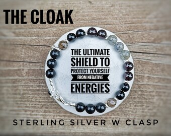 May include: A black, gray, and clear crystal bracelet with a sterling silver clasp. The bracelet has the text "THE ULTIMATE SHIELD TO PROTECT YOURSELF FROM NEGATIVE ENERGIES" on it.
