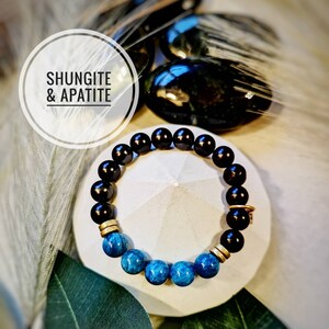 May include: A black and blue beaded bracelet with gold accents. The bracelet is made with shungite and apatite stones. The text "Shungite & Apatite" is visible in the image.