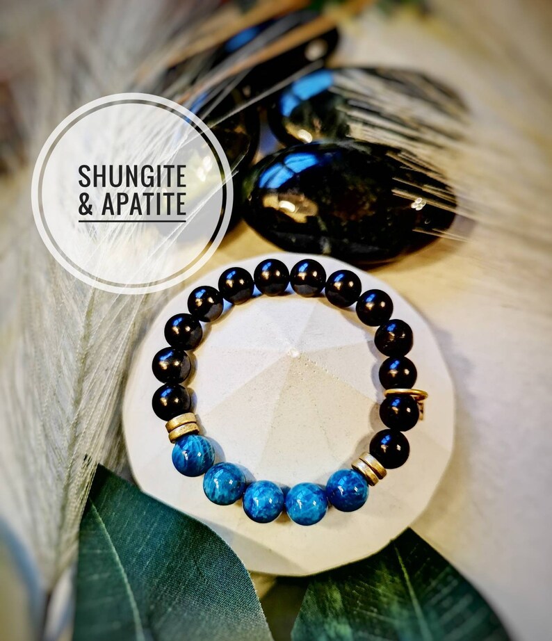 May include: A black and blue beaded bracelet with gold accents. The bracelet is made with shungite and apatite stones. The text "Shungite & Apatite" is visible in the image.