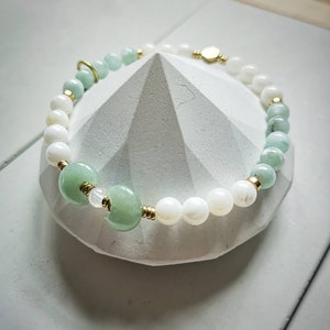 May include: A green and white beaded bracelet with gold accents. The bracelet is made with jade and mother of pearl beads.