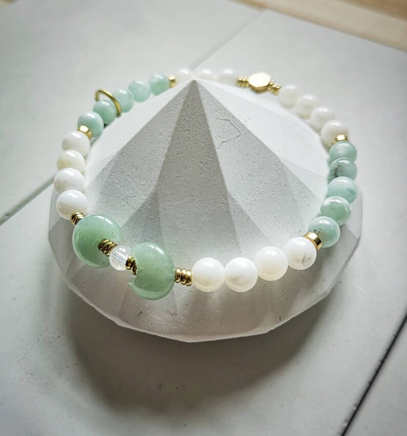 May include: A green and white beaded bracelet with gold accents. The bracelet is made with jade and mother of pearl beads.