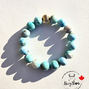 May include: A blue and white gemstone bracelet with a gold bead accent. The bracelet is made of round beads and is approximately 18 cm in length.