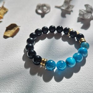 May include: A black and blue beaded bracelet with gold accents. The bracelet is made of round beads and has a stretchy band.