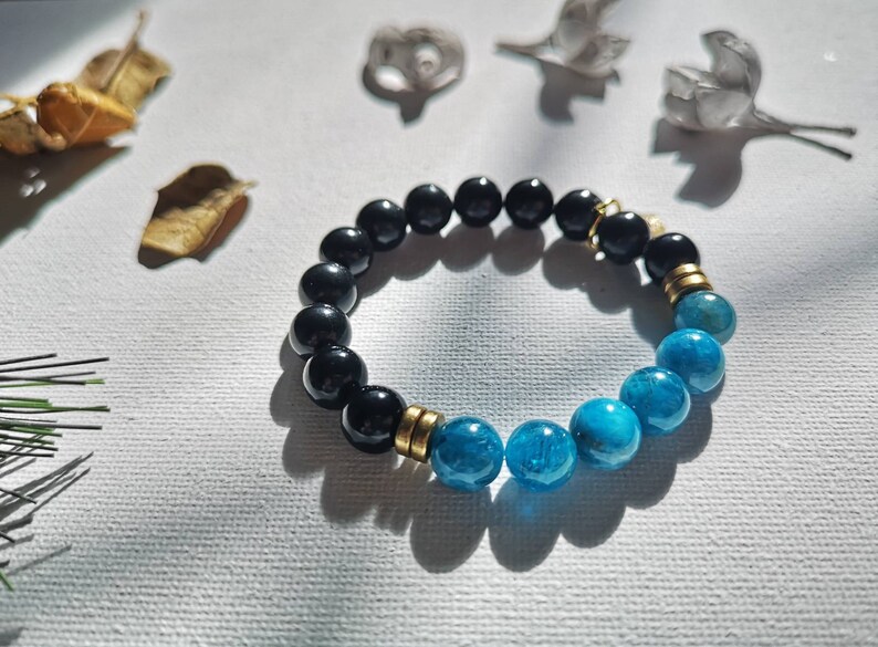 May include: A black and blue beaded bracelet with gold accents. The bracelet is made of round beads and has a stretchy band.