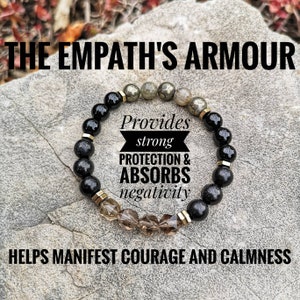 May include: Black and brown beaded bracelet with gold accents. The bracelet has a tag that reads "Provides strong protection & absorbs negativity. Helps manifest courage and calmness."