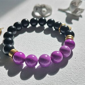 May include: A black and purple beaded bracelet with gold accents. The bracelet is made of round beads and has a simple design.