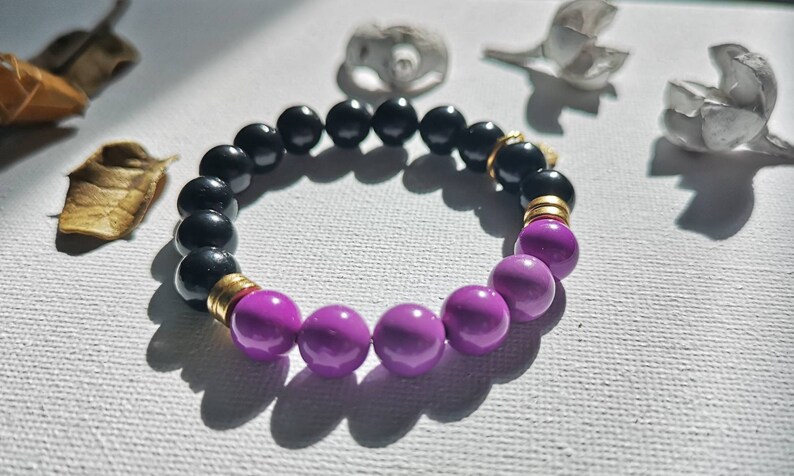 May include: A black and purple beaded bracelet with gold accents. The bracelet is made of round beads and has a simple design.