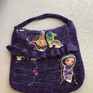 May include: A purple knitted tote bag with a ruffled top. The bag is decorated with fabric appliques of a girl, cats, and birds.