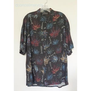 May include: A black short-sleeve button-down shirt featuring a repeating pattern of colorful firework-like bursts in red, blue, and yellow. The fabric is printed with the text "millennium" and "2000" scattered throughout the design.