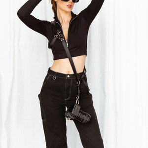 May include: A woman wearing a black long-sleeved top, black trousers, and black sunglasses. She is holding a black camera with a strap around her neck.