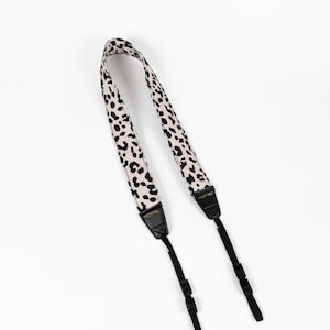 May include: A black and white leopard print camera strap with black adjustable straps and gold hardware.