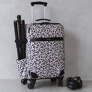Puede incluir: Una maleta de estampado de leopardo blanco y negro con asa y ruedas negras. La maleta tiene un bolsillo negro en el lateral con un trípode negro en su interior. Una cámara negra está sentada en el suelo frente a la maleta.