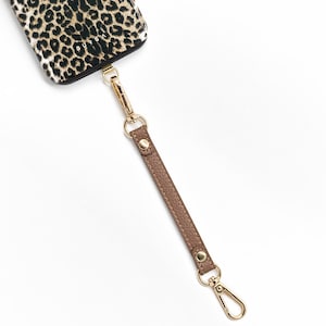 May include: A brown leather phone strap with gold metal clasps. The strap is attached to a leopard print phone case.