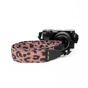 Puede incluir: Una correa de cámara de leopardo marrón y negro con el texto "Violet Mae" en letras doradas.